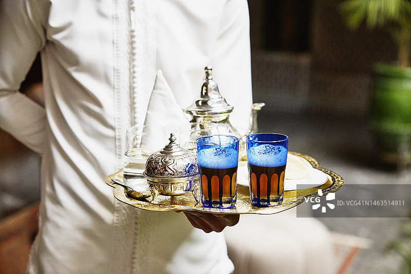 在豪华酒店的托盘上拿着薄荷茶服务的服务员的特写镜头图片素材