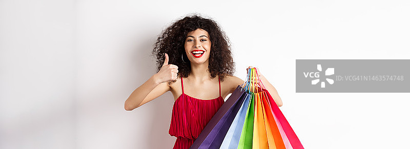 穿着时尚的女人身穿红裙去购物，手提购物袋图片素材