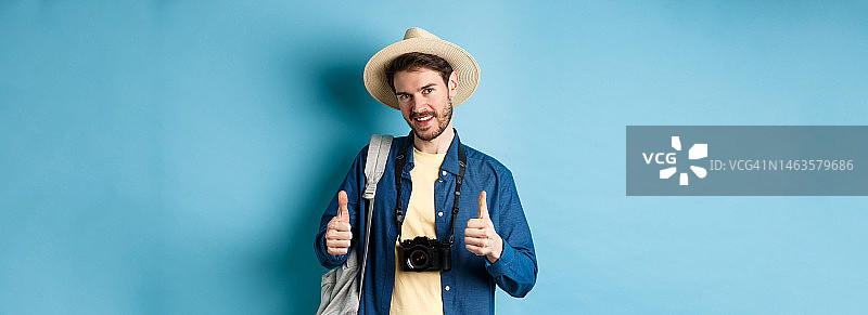 戴着草帽、拿着背包和照片的英俊白人游客图片素材