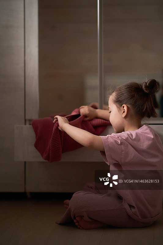 女孩从壁橱抽屉里拿出她最喜欢的粉色毛衣图片素材