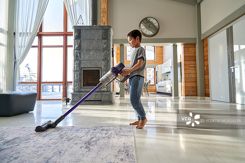 一个韩国男孩用无线吸尘器打扫房子图片素材