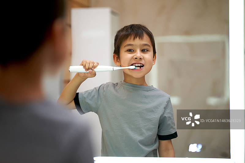 男孩在背光镜子旁用电动牙刷刷牙图片素材