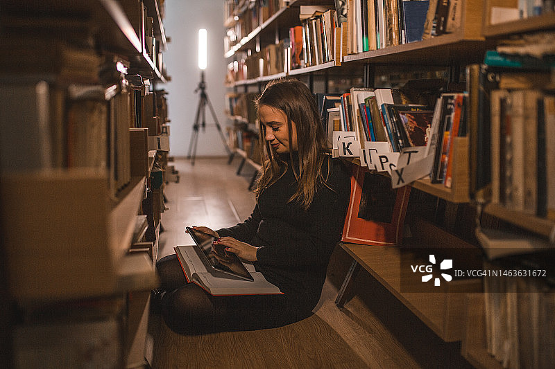 微笑的图书管理员正在图书馆里读书和使用平板电脑图片素材