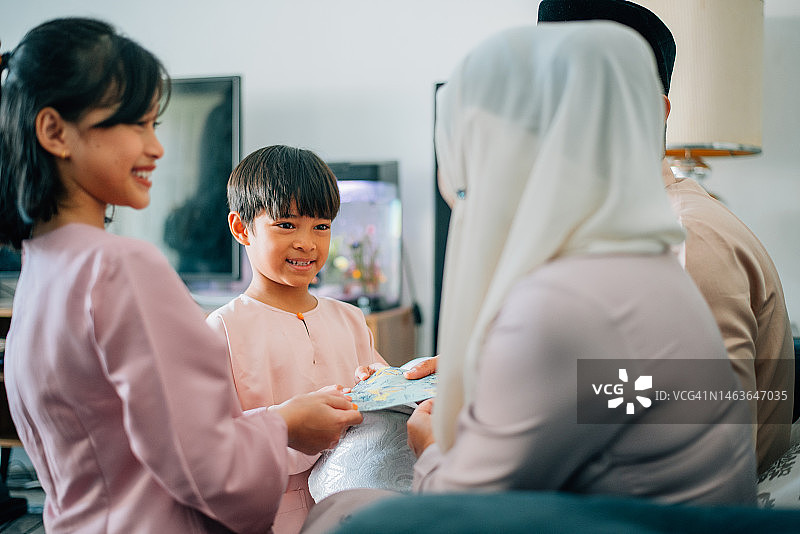 马来西亚穆斯林家庭在客厅里穿着传统服装接受开斋节的红包图片素材