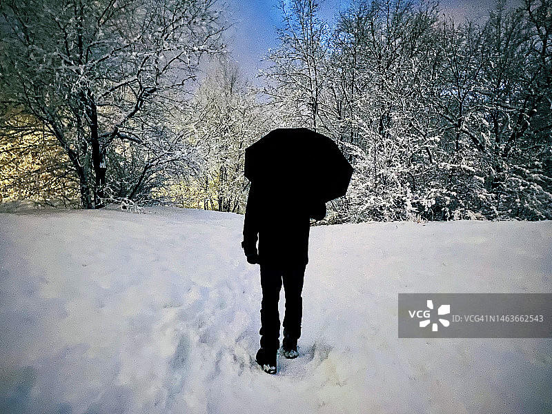 黄昏时分，纽约市中央公园北林区，男子在雪中撑伞走在山坡上图片素材