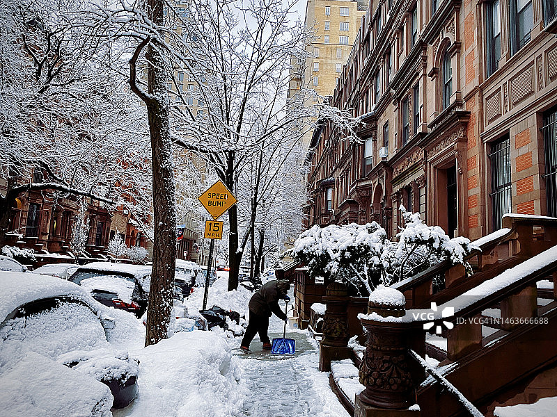 暴风雪中，一个人在纽约市上西区的人行道上铲雪图片素材