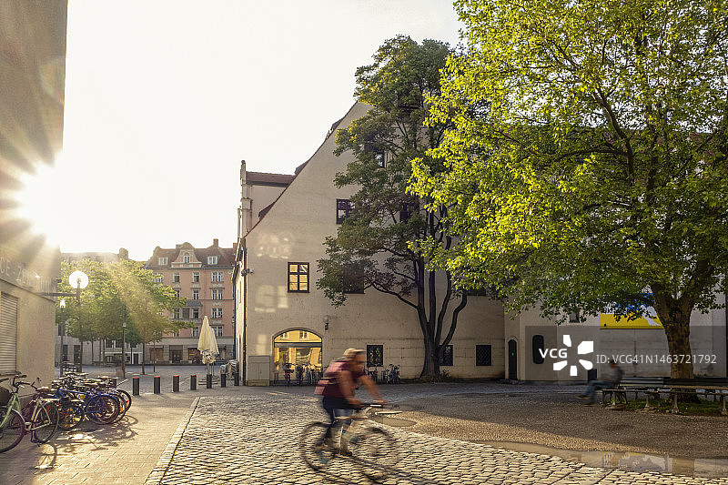 德国巴伐利亚慕尼黑：日落时分骑自行车沿着鹅卵石街道行驶的自行车手图片素材