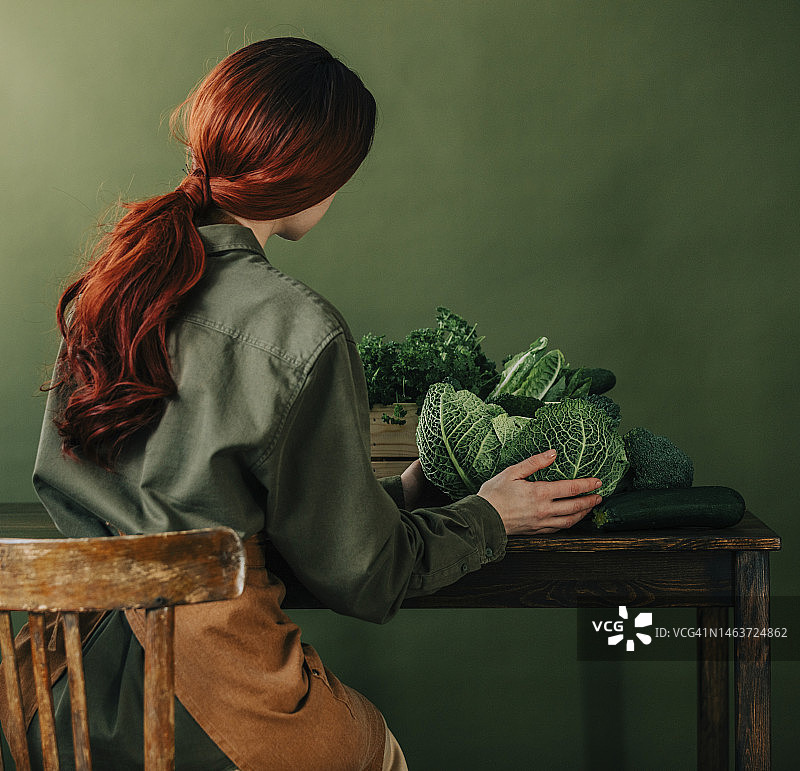 坐在绿墙前桌子旁，手拿新鲜有机蔬菜的女人图片素材