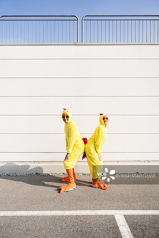 穿着小鸡服装的快乐男人和女人站在墙前图片素材