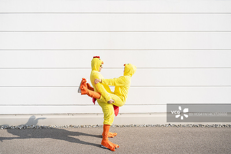 阳光明媚的日子里，身穿小鸡服的欢乐朋友们站在白墙旁图片素材