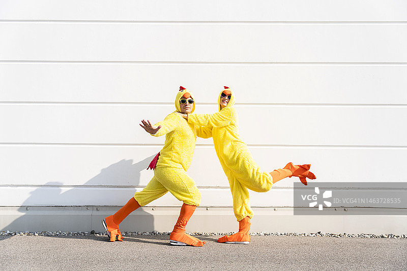 穿着小鸡服装的男人和女人在墙前玩耍图片素材