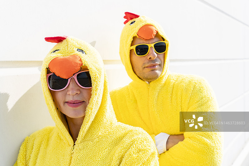 微笑的朋友们戴着小鸡服装和太阳镜靠在墙上图片素材