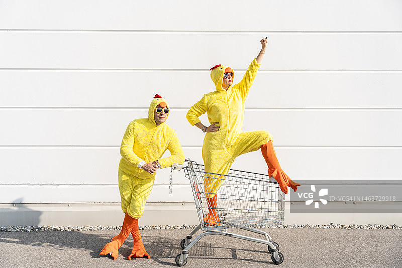 朋友们穿着黄色小鸡服装，推着购物车站在墙前图片素材