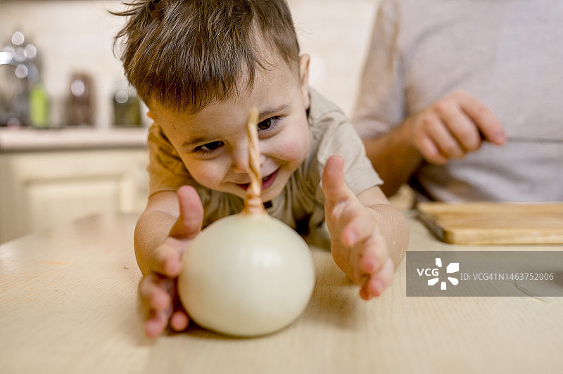 在家中厨房柜台上伸手拿白色洋葱的快乐可爱男孩图片素材