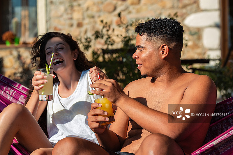 阳光明媚的早晨，朋友们坐在吊床上享用清爽的柑橘汁饮品图片素材