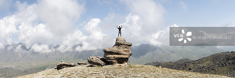 男人站在厄尔布鲁士山，在多云的天空下举起双臂，高加索地区图片素材