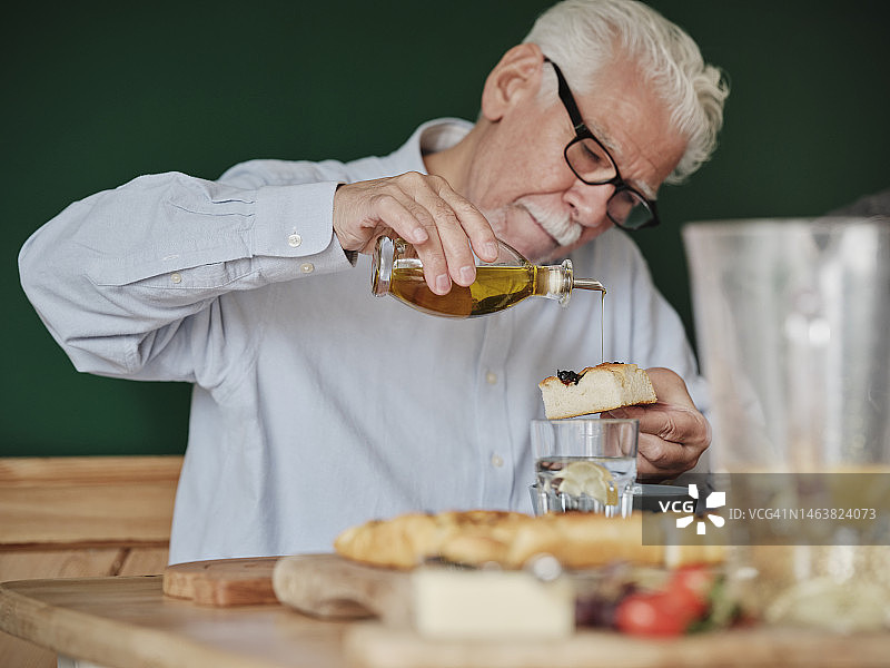 年长的男人在佛卡夏面包上淋橄榄油吃午餐图片素材