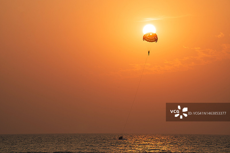 孟加拉国橙色天空下在海上玩滑翔伞的人的剪影图片素材