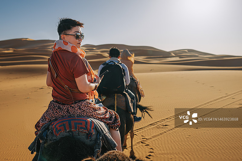 在摩洛哥撒哈拉沙漠日落时行进的中国游客骆驼队图片素材