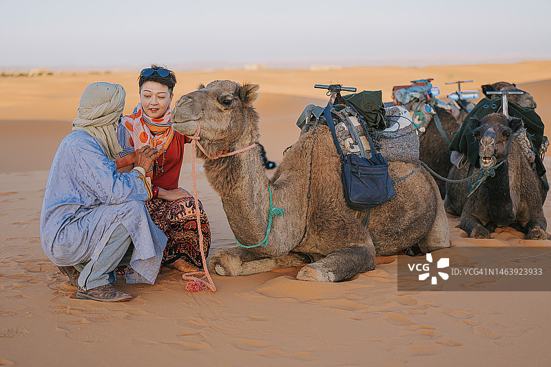 在撒哈拉沙漠，摩洛哥导游向亚洲女游客展示骆驼图片素材