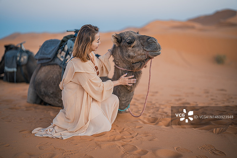 在撒哈拉沙漠触摸骆驼的亚洲女性游客图片素材