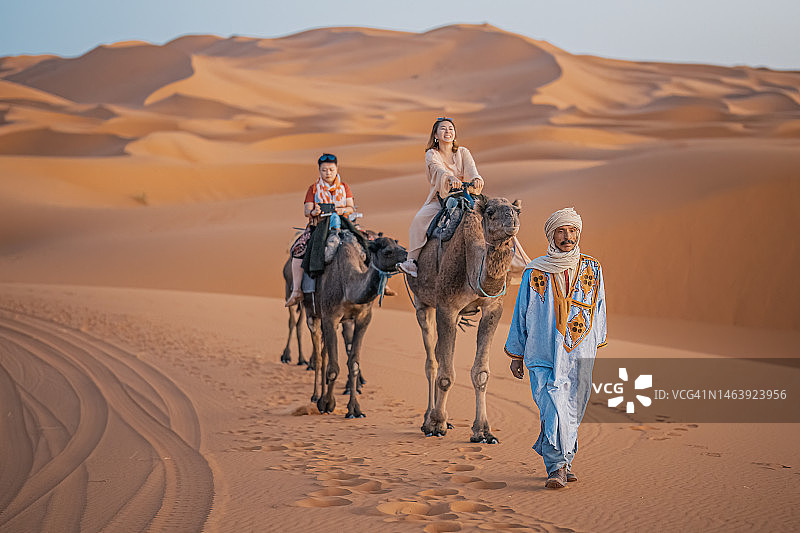 日落时分，中国女性游客在摩洛哥撒哈拉沙漠体验骆驼之旅图片素材
