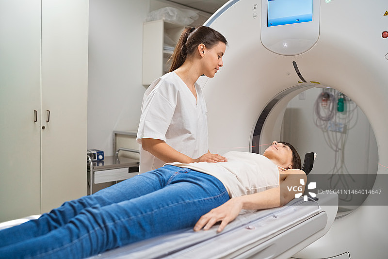 女病人在医疗检查室里躺在核磁共振扫描仪上，由女医护人员陪同图片素材