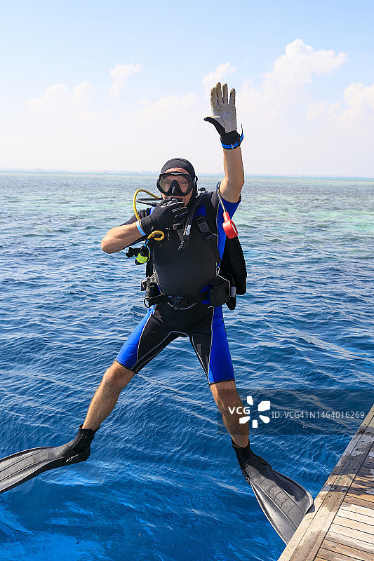 准备水肺潜水的中年英俊男运动员潜水员，跳入美丽的热带蓝色海洋，背景是珊瑚礁。水上运动图片素材