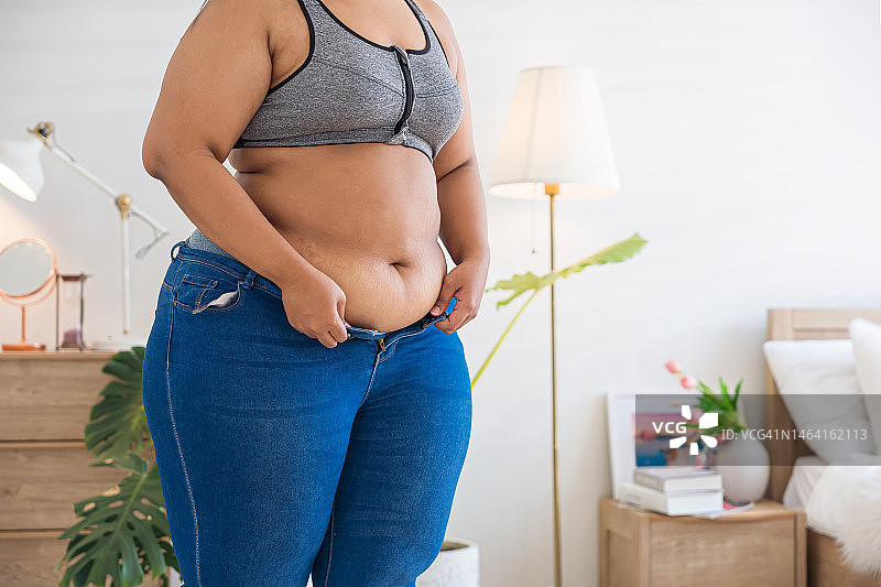 身材偏胖的女人试图系上紧绷的牛仔裤图片素材