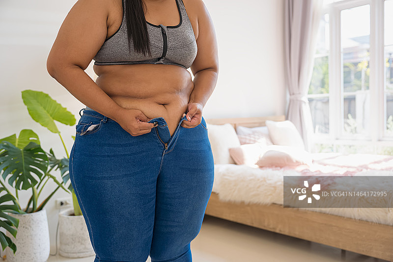 身材偏胖的女人试图系上紧绷的牛仔裤图片素材