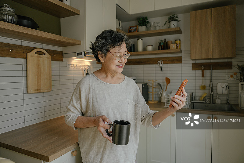 亚洲老年妇女通过视频电话与女儿见面，手拿咖啡杯图片素材