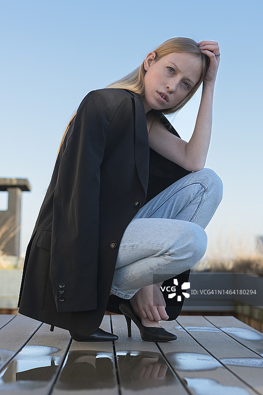 年轻女子蹲在露台上，背景是晴朗的天空，布鲁塞尔，比利时图片素材