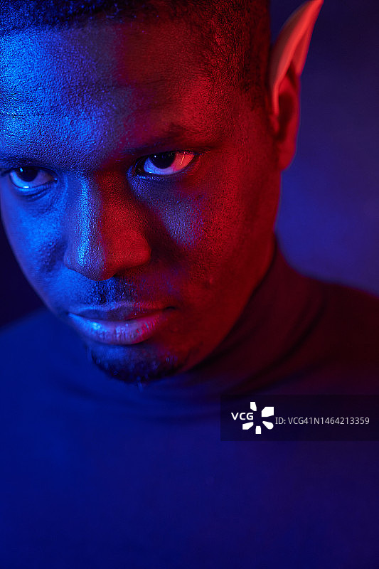 戴着精灵耳朵和霓虹灯的蓝红色黑人男子艺术肖像，深色背景上有复制空间图片素材