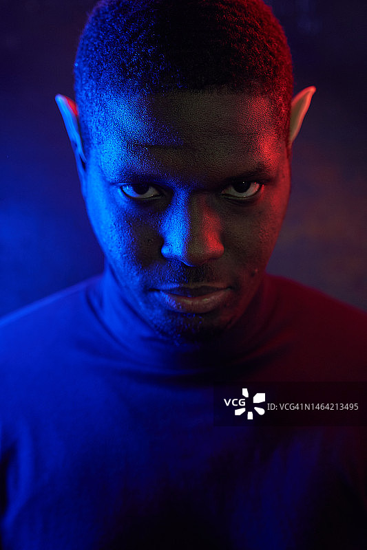 戴着精灵耳朵和霓虹灯的蓝红色黑人男子艺术肖像，深色背景上有复制空间图片素材