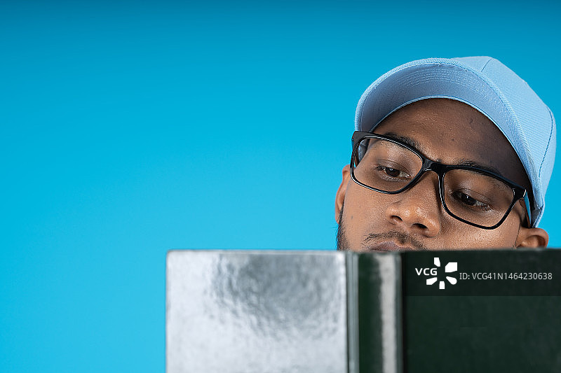 戴着帽子和眼镜的年轻非洲裔男人正在读一本深色精装书图片素材