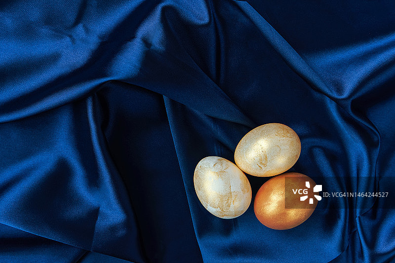 蓝色背景上的三个白色和金色复活节彩蛋图片素材