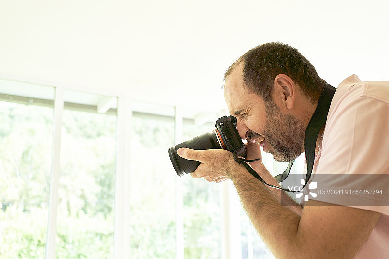 男子身穿休闲装站在屋内，面带微笑地用相机拍照的侧面图图片素材