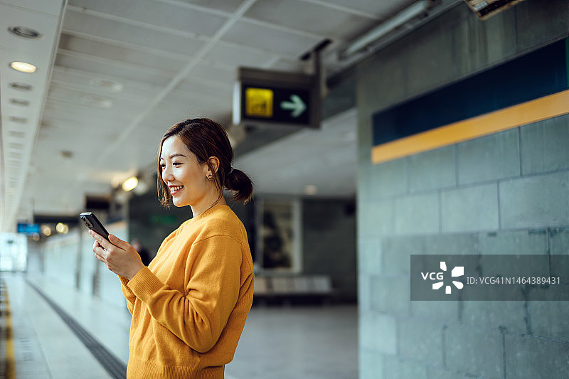 亚洲年轻女人地铁站玩手机图片素材