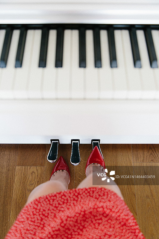 钢琴踏板旁穿红裙和红色高跟鞋的女子。腿部和白色钢琴的俯视图图片素材