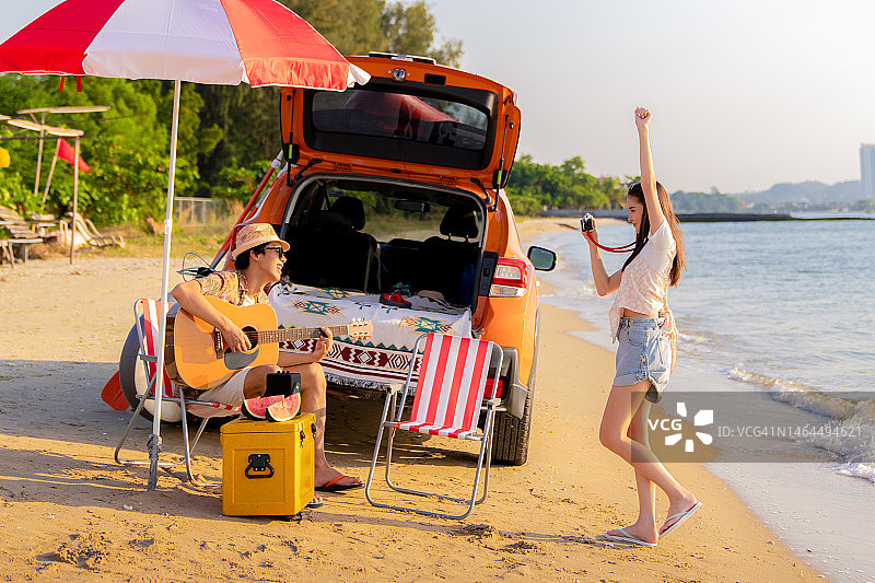 年轻情侣在海滩边弹吉他，女友用相机拍照图片素材