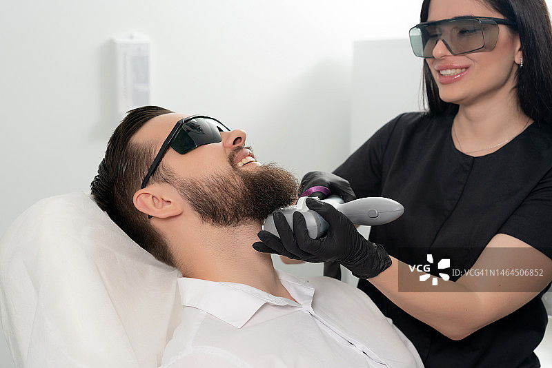 年轻的络腮胡男人接受专业激光面部护理图片素材