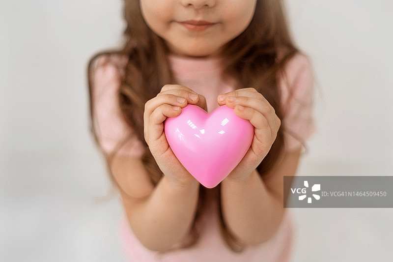 可爱的小女孩手握粉色爱心站在白色背景上图片素材