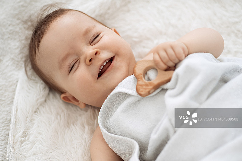 可爱有趣的小宝宝在用木制磨牙器后在床上休息图片素材