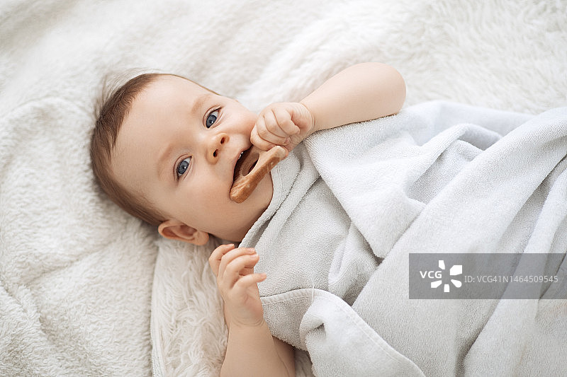 可爱有趣的小宝宝在用木制磨牙器后在床上休息图片素材