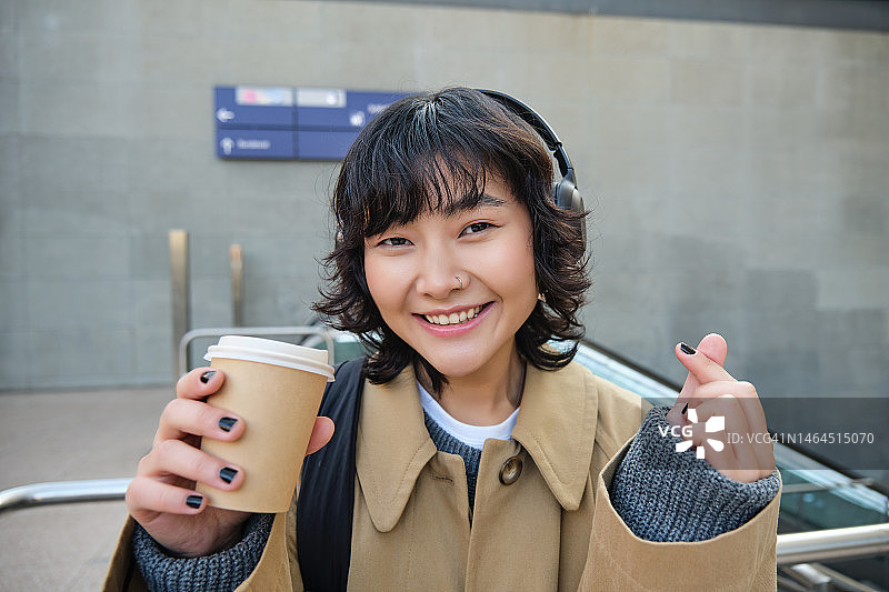 戴着耳机、喝着咖啡的时尚亚洲女性肖像图片素材