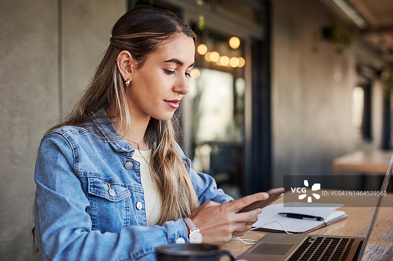 在咖啡馆使用笔记本电脑或手机进行电子学习的女学生图片素材