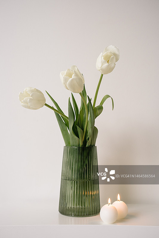 绿玻璃花瓶中的白色郁金香和白色桌子上的蜡烛图片素材