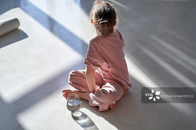 穿着粉色衣服的女孩坐在大理石地板上，旁边有一杯阳光下的水图片素材