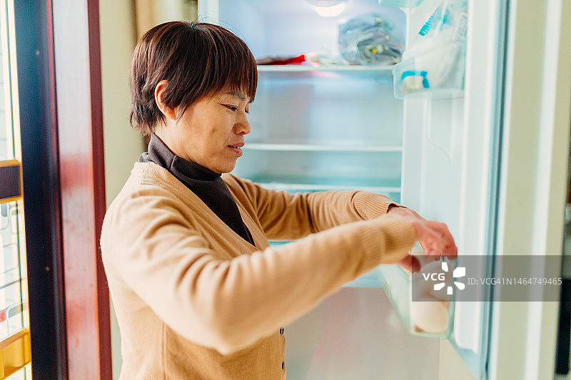 从冰箱里拿出鸡蛋准备早餐的中年妇女 - 健康生活方式，家庭生活图片素材