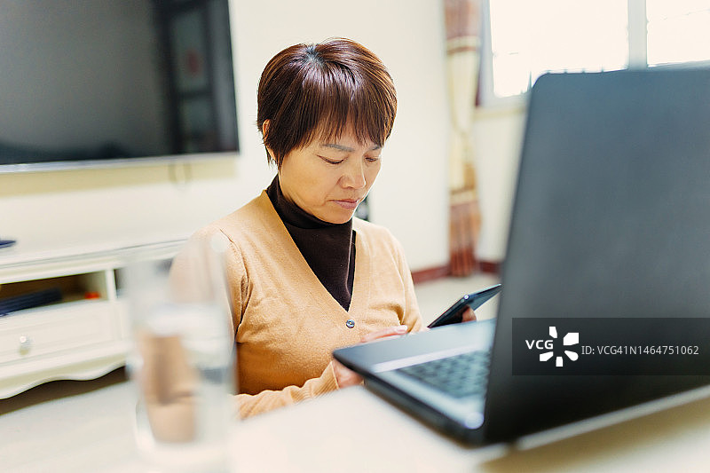 中年妇女在家用手机购物——科技与生活、信用卡、银行和支付概念图片素材